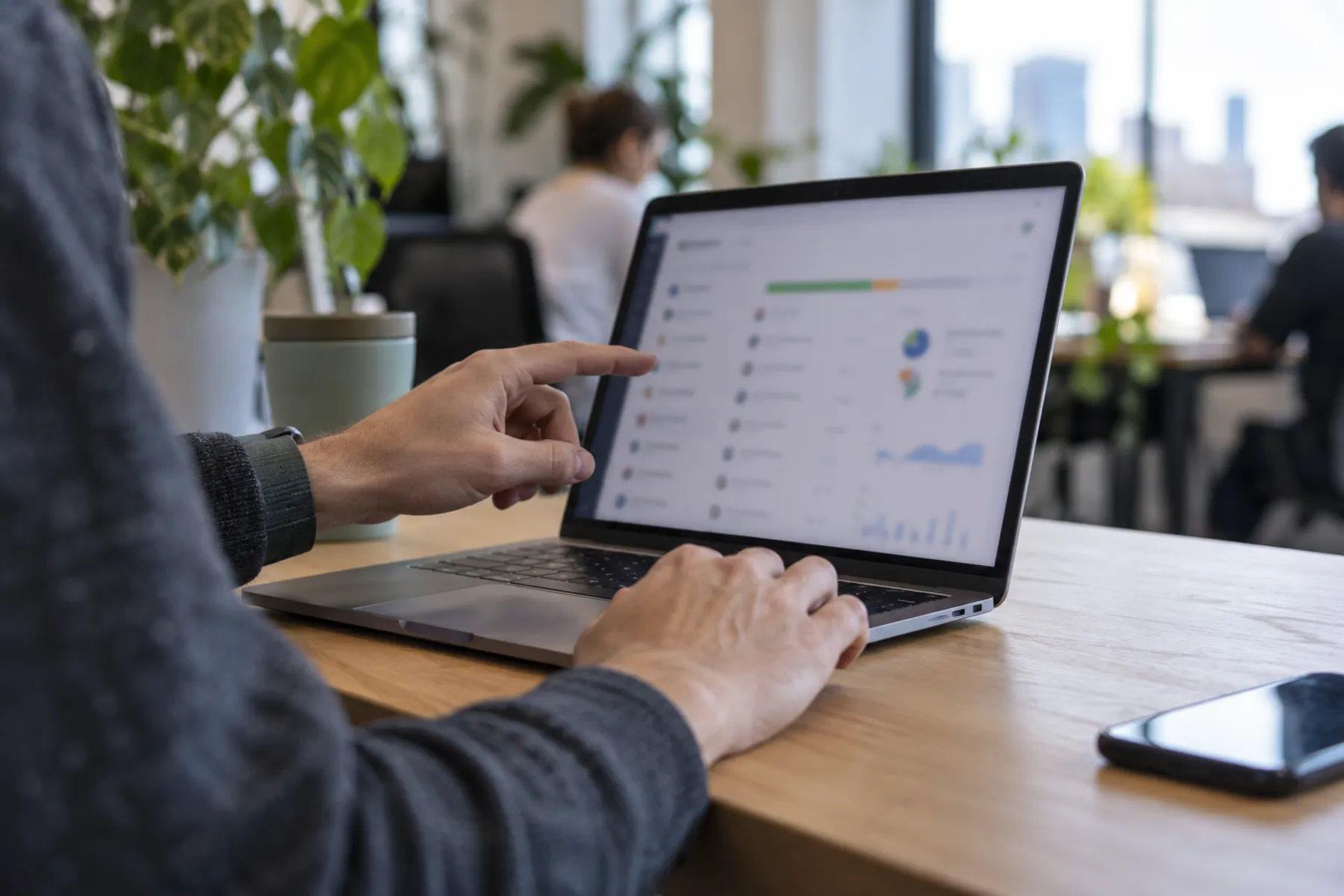 An anonymous office worker uses a laptop trackpad and points towards a blurred activity display while reviewing an automated payment workflow.