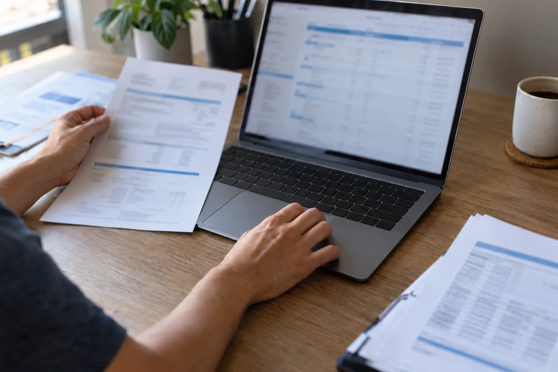 A staff member reviews extracted document fields on a laptop beside face-up invoices and forms, with only their hands visible.